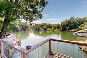 A lakeside property with a wooden deck, a dock, and a view of the lake and surrounding trees. - Lake Lure Lakefront House, Private Dock, Multiple Decks, Kayaks, Mountain Views, Gameroom (Lake Lure)