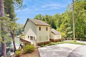 A two-story house with a sloped roof, a front porch, and a driveway leading to a dock. - Lake Lure Lakefront House, Private Dock, Multiple Decks, Kayaks, Mountain Views, Gameroom (Lake Lure)
