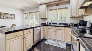 A modern kitchen with light wood cabinets, a black countertop, and stainless steel appliances. - Lake Lure Lakefront House, Private Dock, Multiple Decks, Kayaks, Mountain Views, Gameroom (Lake Lure)