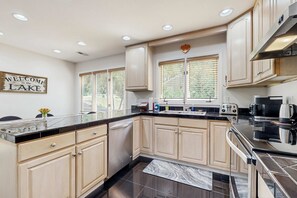 A modern kitchen with light wood cabinets, a black countertop, and stainless steel appliances. - Lake Lure Lakefront House, Private Dock, Multiple Decks, Kayaks, Mountain Views, Gameroom (Lake Lure)