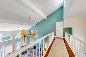 A spacious interior with a high ceiling, a staircase with white railings, and a view of the outdoors through a large window. - Lake Lure Lakefront House, Private Dock, Multiple Decks, Kayaks, Mountain Views, Gameroom (Lake Lure)