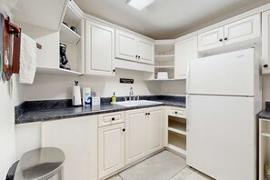 A kitchen with white cabinets, a black marble countertop, a white refrigerator, and a sign that says 'Jesus knows me This I love.' - Lake Lure Lakefront House, Private Dock, Multiple Decks, Kayaks, Mountain Views, Gameroom (Lake Lure)
