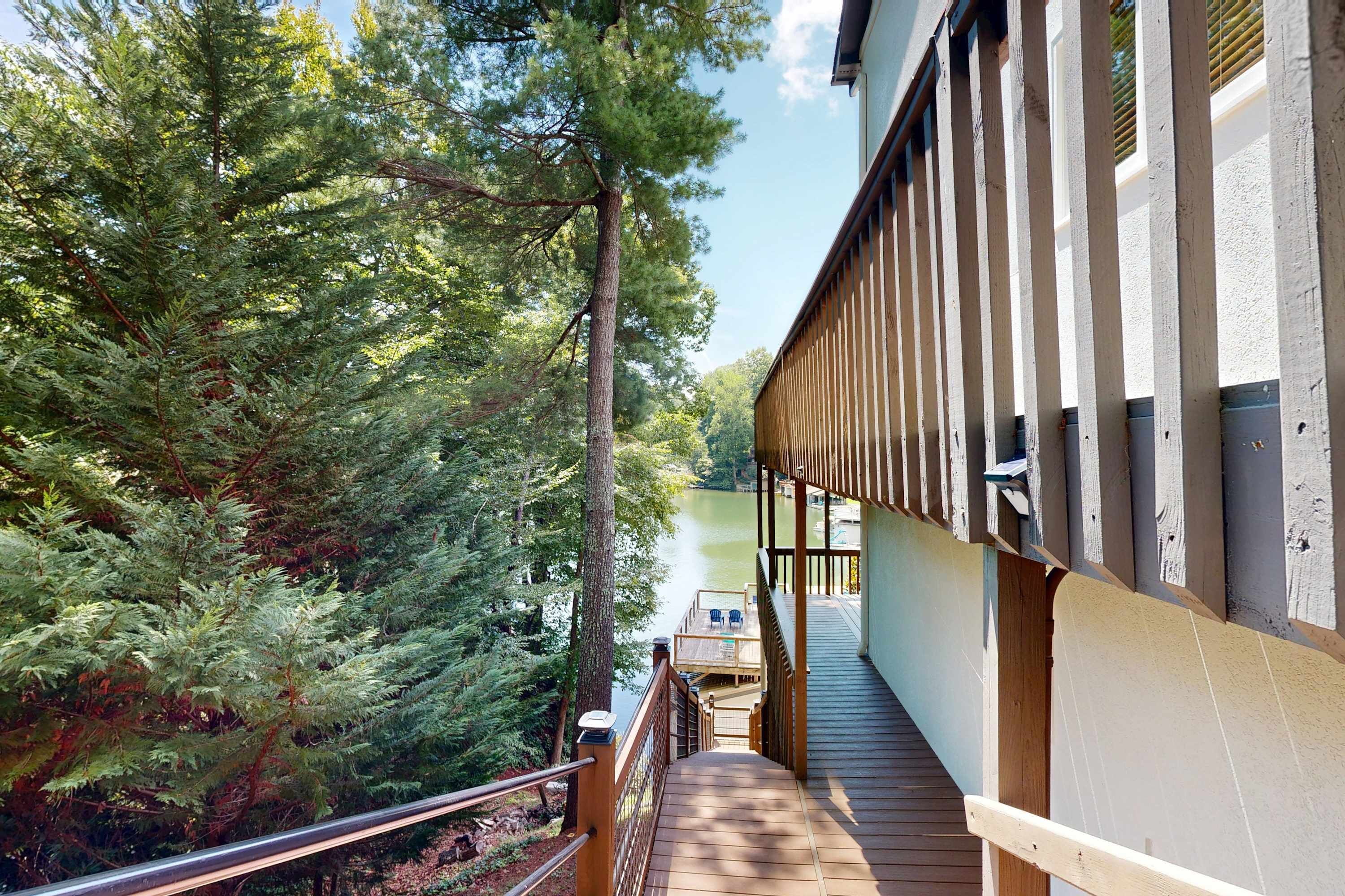 A wooden deck leading to a building with a view of a lake and dense trees.