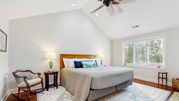 A bedroom with a bed, two bedside lamps, a rocking chair, a window with blinds, and a ceiling fan. - Lake Lure Lakefront House, Private Dock, Multiple Decks, Kayaks, Mountain Views, Gameroom (Lake Lure)