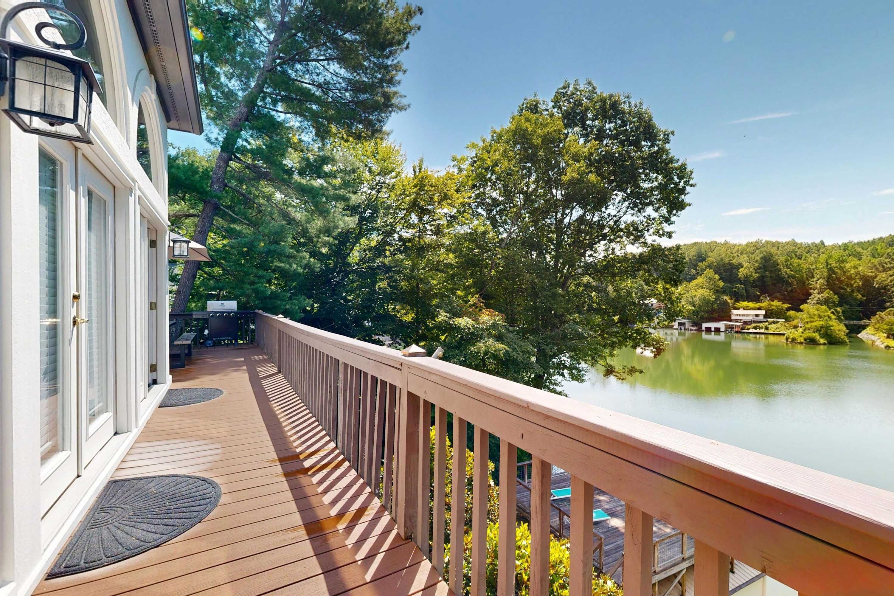 Une terrasse en bois avec une rambarde donnant sur un lac, entourée d’arbres.