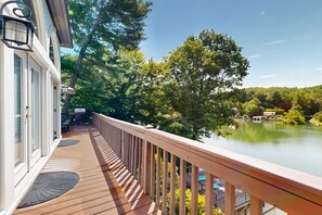 A wooden deck with a railing overlooking a lake, surrounded by trees. - Lake Lure Lakefront House, Private Dock, Multiple Decks, Kayaks, Mountain Views, Gameroom (Lake Lure)