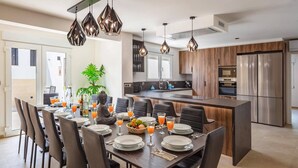 Une cuisine moderne dotée d’un îlot central, d’appareils électroménagers en acier inoxydable et de luminaires suspendus.