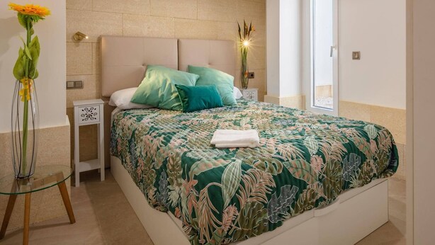 Une chambre à coucher avec un lit, une table de chevet, une table en verre et un vase rempli de fleurs.