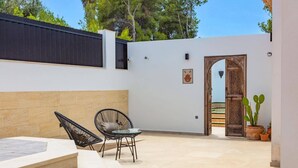 Une cour avec un mur blanc, une porte en bois et un pot de fleurs.