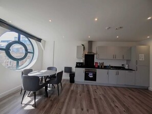 Een moderne keuken met een rond raam, een zithoek met een tafel en stoelen, en een stadsgezicht door het raam.