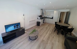 A modern living room with a flat-screen TV, a round coffee table with a plant, and a dining area with a table and chairs. - City Centre One Bedroom Apartments (Liverpool)