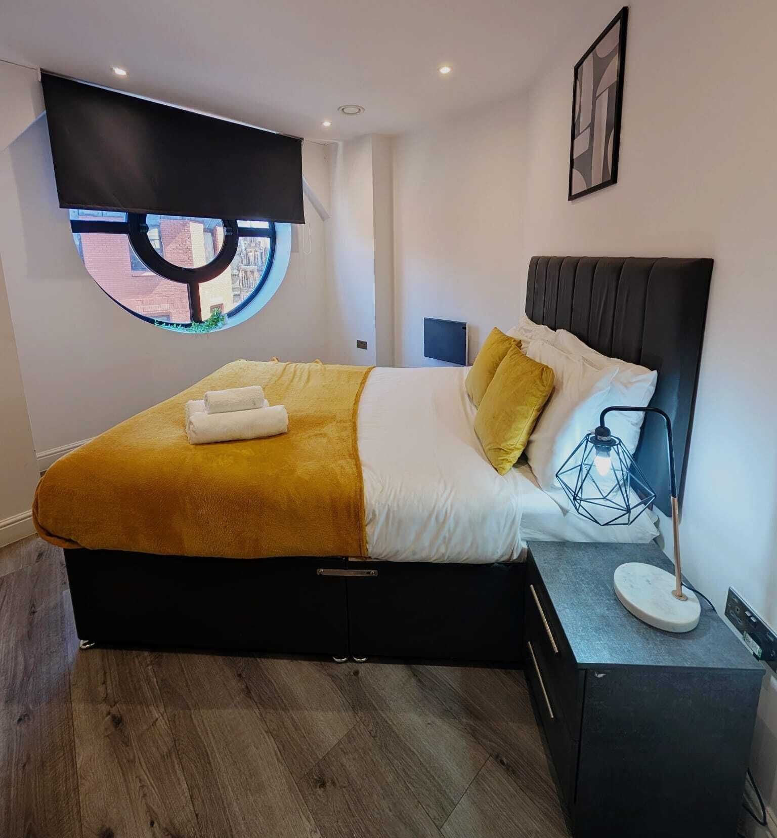 Quarto moderno com cama, janela redonda, luminária de cabeceira e mesa de cabeceira.