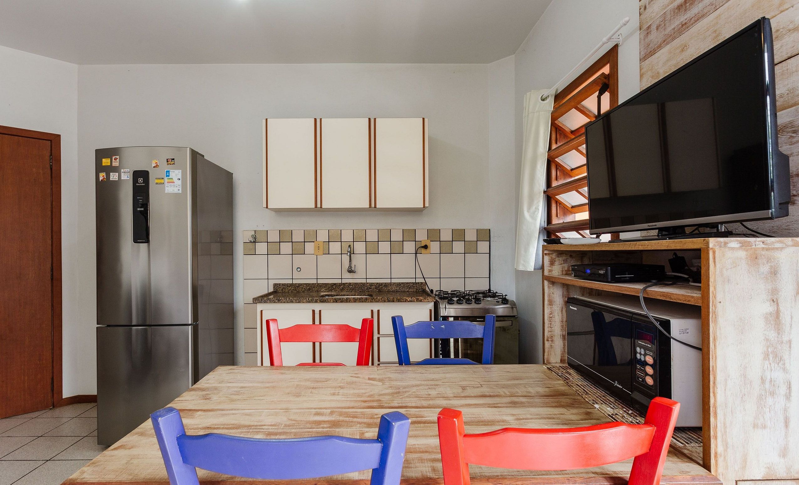 Une cuisine compacte équipée d’un réfrigérateur, d’un four à micro-ondes, d’une cuisinière et d’un téléviseur à écran plat.