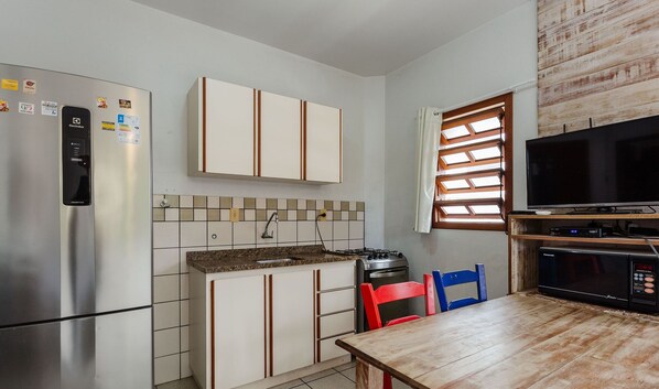 A compact kitchen with a refrigerator, stove, microwave, and a dining area with chairs. - Comfortable Apt 270m From the Beach Stcy101 (Florianópolis)