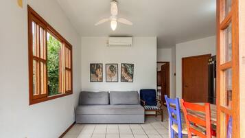 Una habitación con un sofá gris, un ventilador de techo y tres obras de arte con hojas enmarcadas en la pared.
