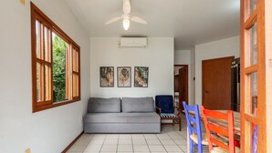 Una habitación con un sofá gris, un ventilador de techo y tres obras de arte con hojas enmarcadas en la pared.