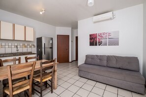 Una cocina moderna con armarios blancos, un refrigerador de acero inoxidable, una mesa de comedor con sillas de madera y un sofá gris.