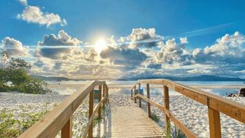 Un paseo marítimo de madera que lleva a una playa con cielo despejado y sol.