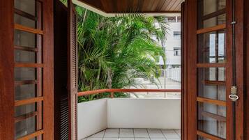 A corner balcony with wooden doors and a view of a building in the background.