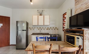 A compact kitchen with a refrigerator, a microwave, a dining table with chairs, a TV, and cabinets above the counter. - Nice Apartment 270m From the Beach Stcy201 (Florianópolis)