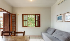 A room with a wooden table, two chairs, a grey sofa, a window with a view of trees, and two framed pictures on the wall. - Nice Apartment 270m From the Beach Stcy201 (Florianópolis)