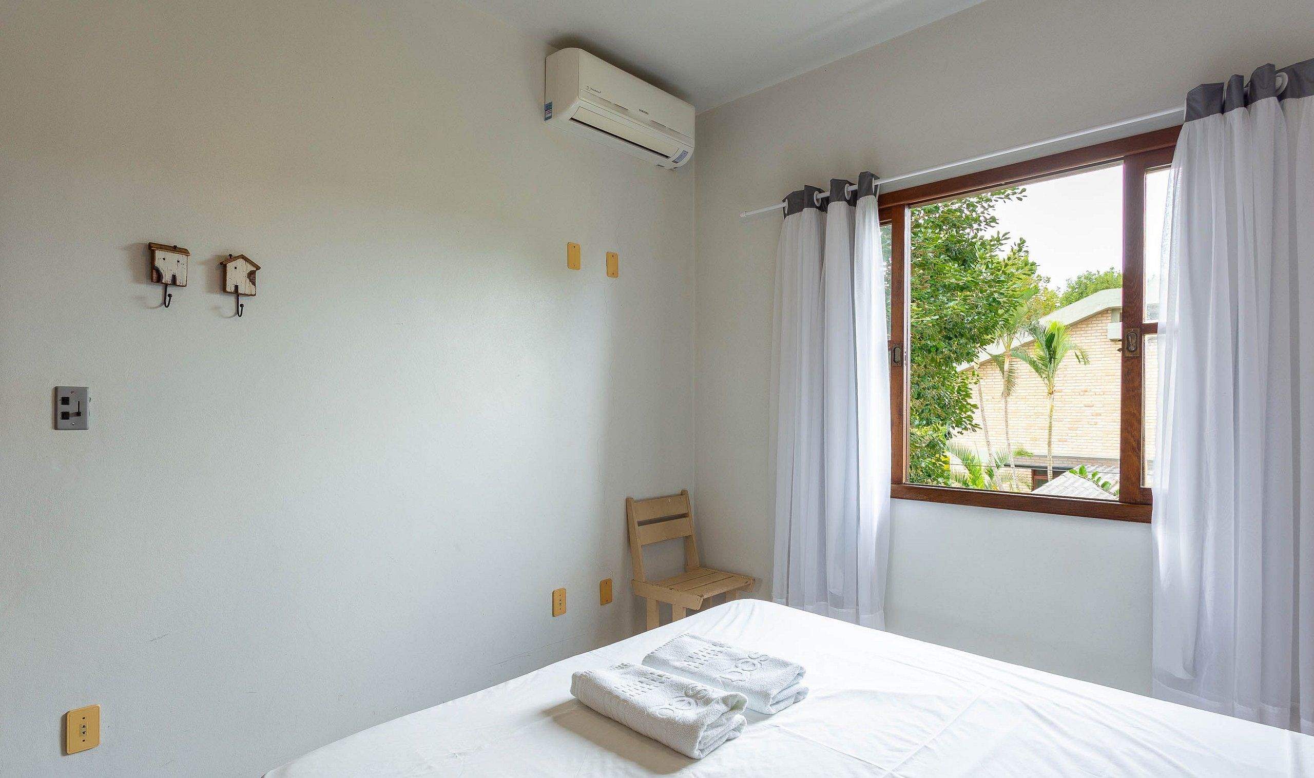 Un dormitorio con cama, una silla, aire acondicionado y una ventana con cortinas.