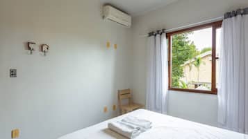 A bedroom with a bed, a chair, an air conditioning unit, and a window with curtains.