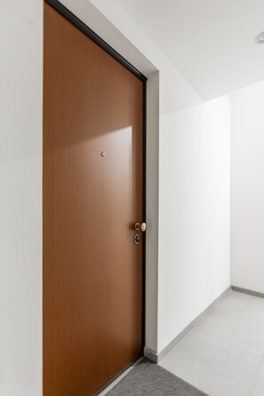 A closed wooden door with a handle and a keyhole, leading to a hallway with white walls and a grey carpet. - San Gervasio Apartment by Wonderful Italy (Bologna)