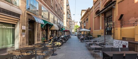A narrow street with outdoor seating and tables, lined with buildings on both sides.
