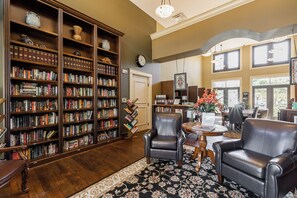 A library with bookshelves, a leather chair, a table with a vase of flowers, and a clock on the wall. - 3bed/2.5Resort-style Paseo QUAD home w/semi-private pool. (Fort Myers)