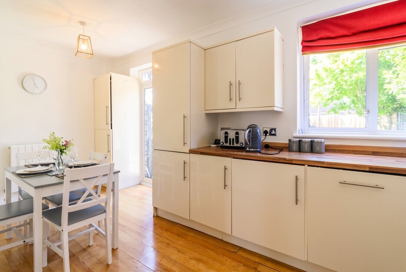 A kitchen with white cabinets, a wooden countertop, and a window with red curtains.