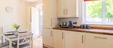 A kitchen with white cabinets, a wooden countertop, and a window with red curtains.