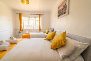 Ein Hotelzimmer mit zwei Betten, einem fensterbelaubten Fenster, einem Bild an der Wand und Handtüchern auf dem Bett.
