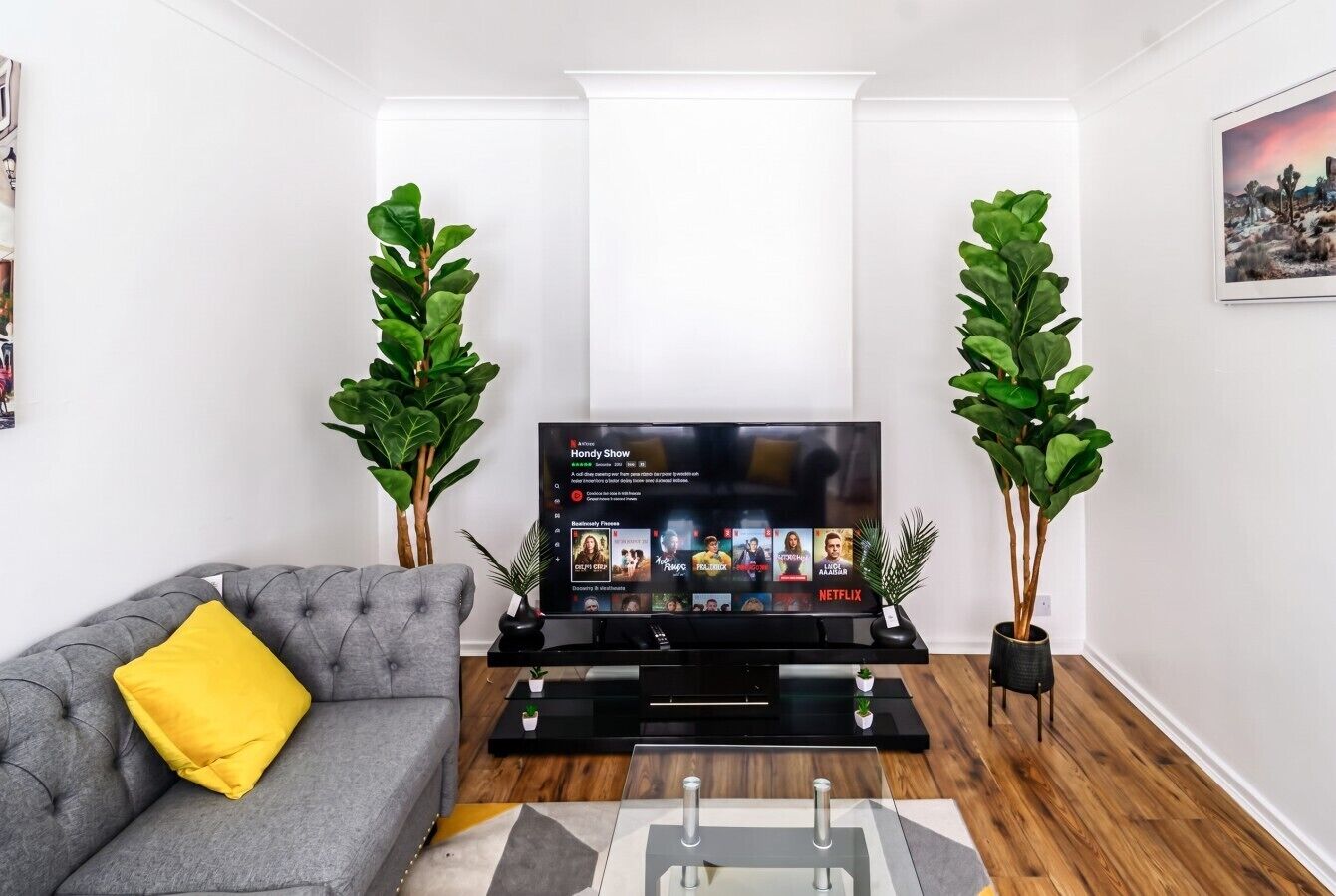 Un salon moderne avec un canapé gris, un téléviseur à écran plat et deux plantes en pot.