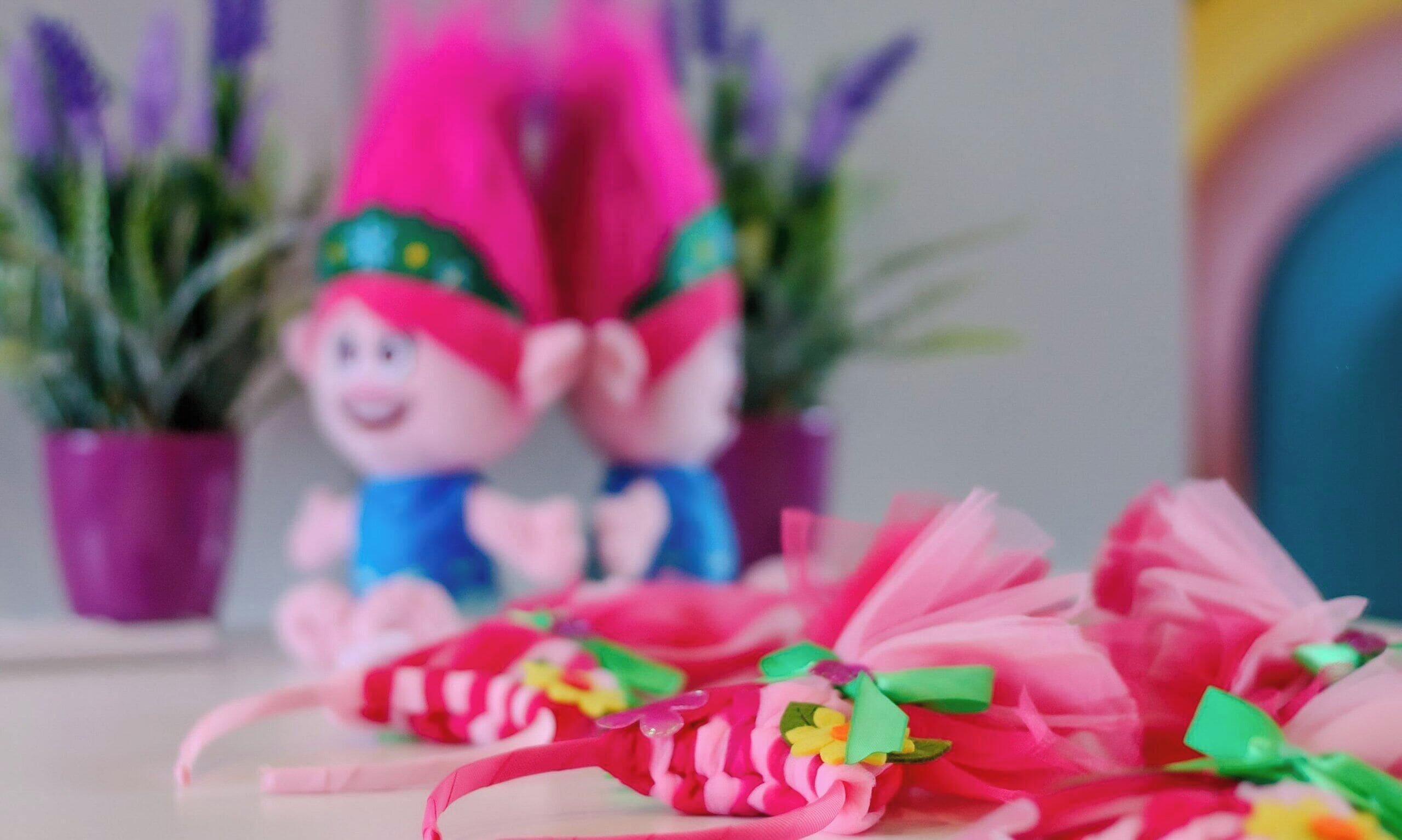 A decorative scene with a figure in a red hat and blue outfit, surrounded by pink and green floral arrangements.