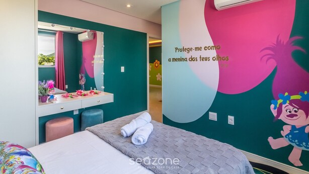 A bedroom with a bed, a vanity with a mirror, and a wall with a cartoon character. - 2-bedrthemed Rainbow Ap With Barbecue Obp0301 (Penha)