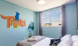 Quarto com cama, janela com cortinas e um mural da Trolls na parede.