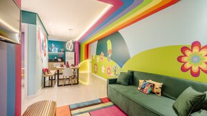 A vibrant children's room with a sofa, colorful wall art, and a kitchen area. - 2-bedrthemed Rainbow Ap With Barbecue Obp0301 (Penha)
