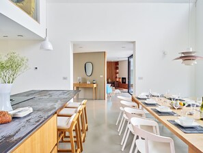 A modern dining area with a long table, multiple chairs, and a central island with a bench. - The Chatterbox at Waterloo Farm (Halesworth)
