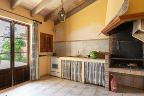 A kitchen with a built-in grill, a window with curtains, and a wooden door. - Son Idò by Rentallorca Mallorcan essence amidst the gardens (Muro)