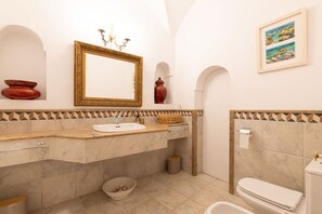 Ein Badezimmer mit Marmorwaschbecken, einem goldfarbenen Spiegel, einer roten Vase und einem Bild an der Wand.