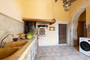 A kitchen with a sink, a large watermelon, a washing machine, and a wooden door. - Son Idò by Rentallorca (Muro)