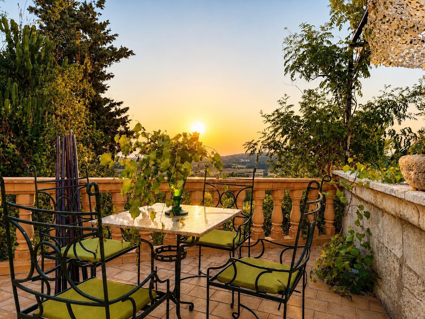 An outdoor patio with a table and chairs, surrounded by greenery and a view of the sunset.