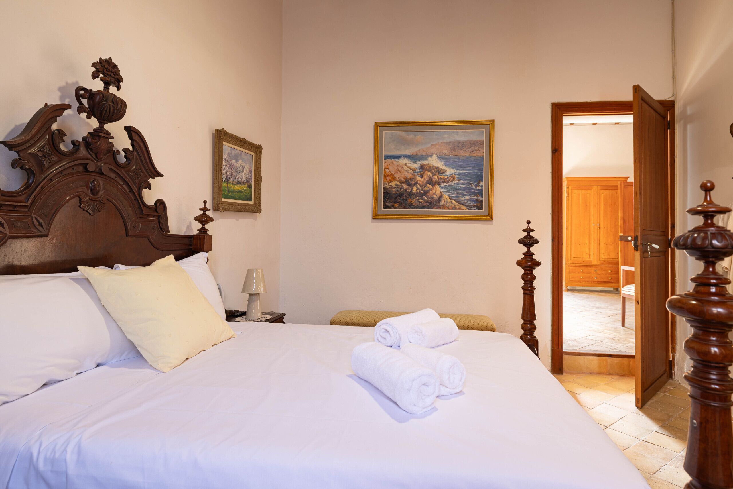 Una cama bien hecha con sábanas blancas, un cabecero de madera y un cuadro con una escena costera en la pared.