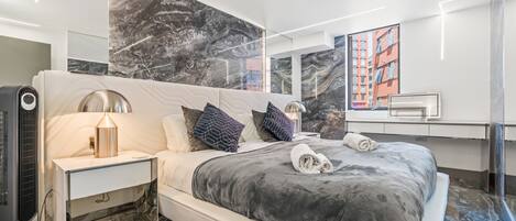 A modern bedroom with a large bed, a nightstand, a lamp, and a mirror.