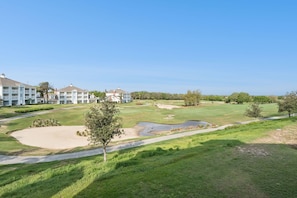 Ein Golfplatz mit Bunkern, einem Teich und einem Gebäudekomplex im Hintergrund.