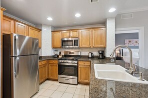 A modern kitchen with stainless steel appliances, wooden cabinets, granite countertops, and a built-in oven. - Epic Reunion Resort Escape - Near Disney & Heritage Pool (Kissimmee)
