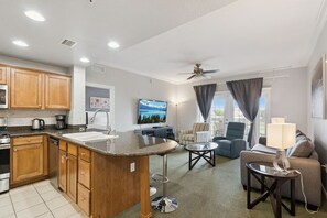 A modern kitchen with a bar area, a dining table, and a living room with a sofa and a TV. - Epic Reunion Resort Escape - Near Disney & Heritage Pool (Kissimmee)