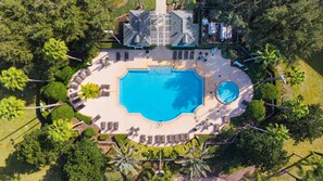 Eine Vogelperspektive zeigt ein Resort mit einem großen zentralen Pool, Liegestühlen und Palmen.