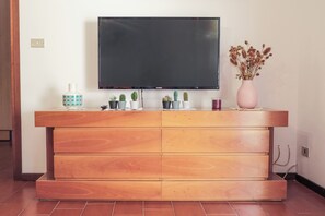 Ein Holzunterhaltungsschrank mit einem flachbildfernseher darüber, eine Vase mit Trockenblumen und einige kleine Topfpflanzen.
